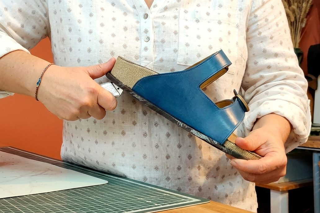Sandale en cours de fabrication : Delphine Rouchon travaille le bord de la semelle, une forme de chaussure posée sur l'établi